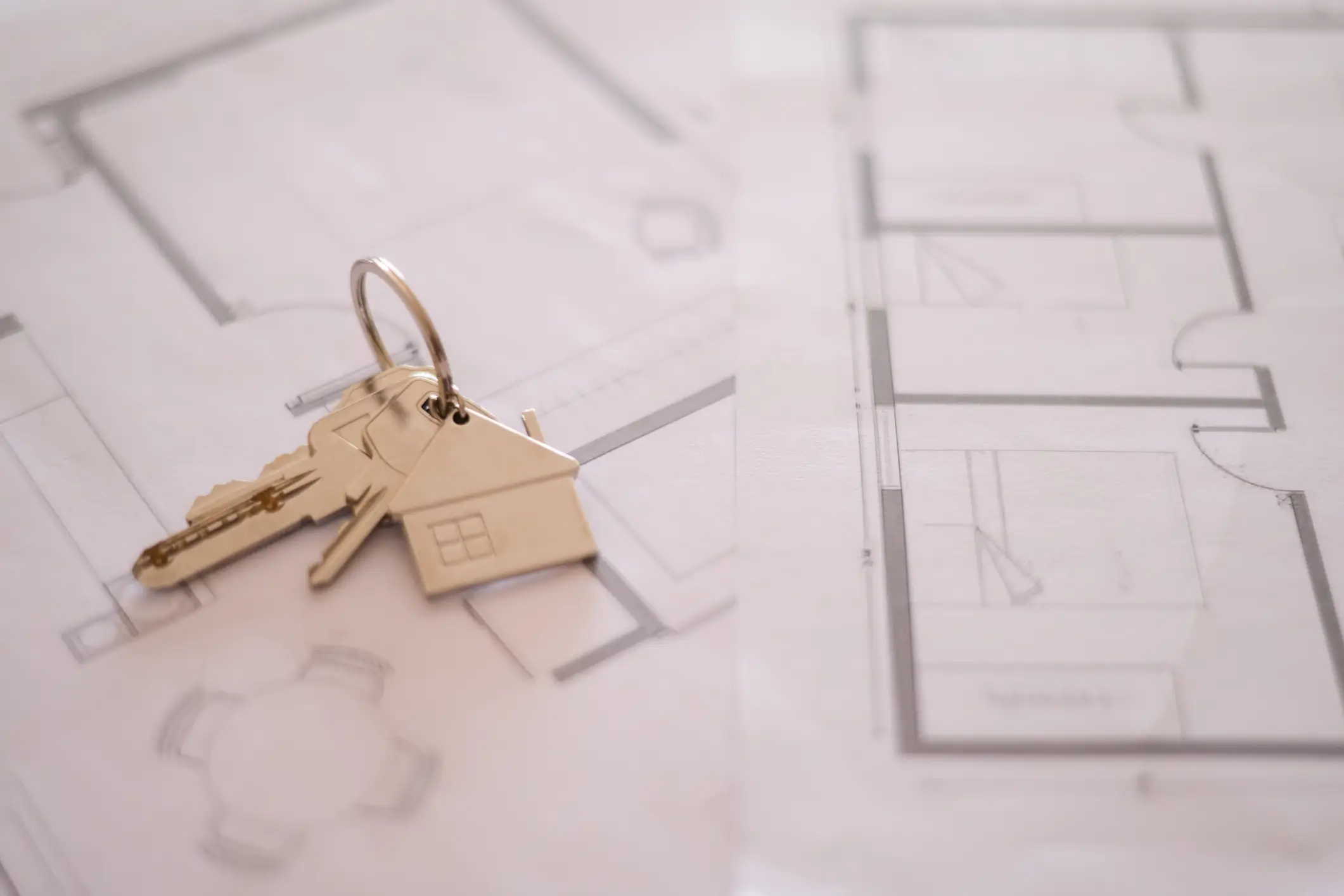 House shaped keychain with keys is lying on architectural plans, representing the concept of buying, selling, renting, or building a new home